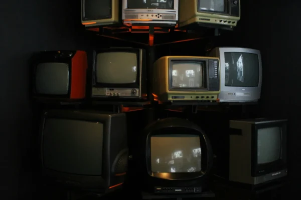 Stack of vintage television sets arranged on shelves against a dark background, displaying various sizes and styles from different eras.