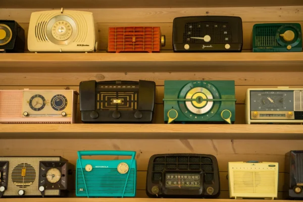 Collection of vintage radios displayed on wooden shelves, featuring various colors and styles from mid-20th century.