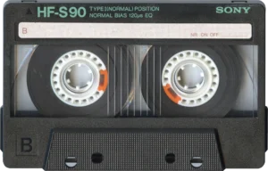 Sony HF-S90 cassette tape with dual reels and orange safety tabs visible against black casing.