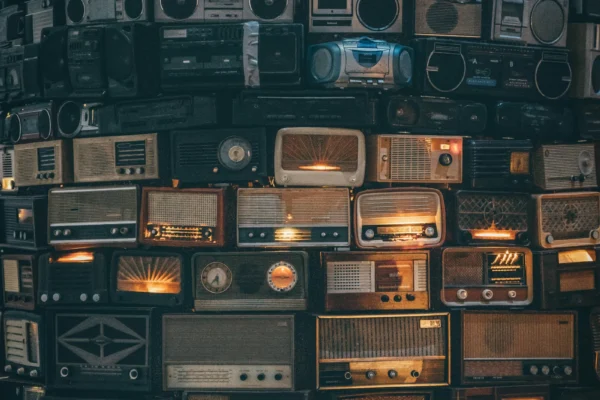 Overhead view of vintage radios and boomboxes arranged in rows, some with illuminated dials and displays glowing orange and blue.